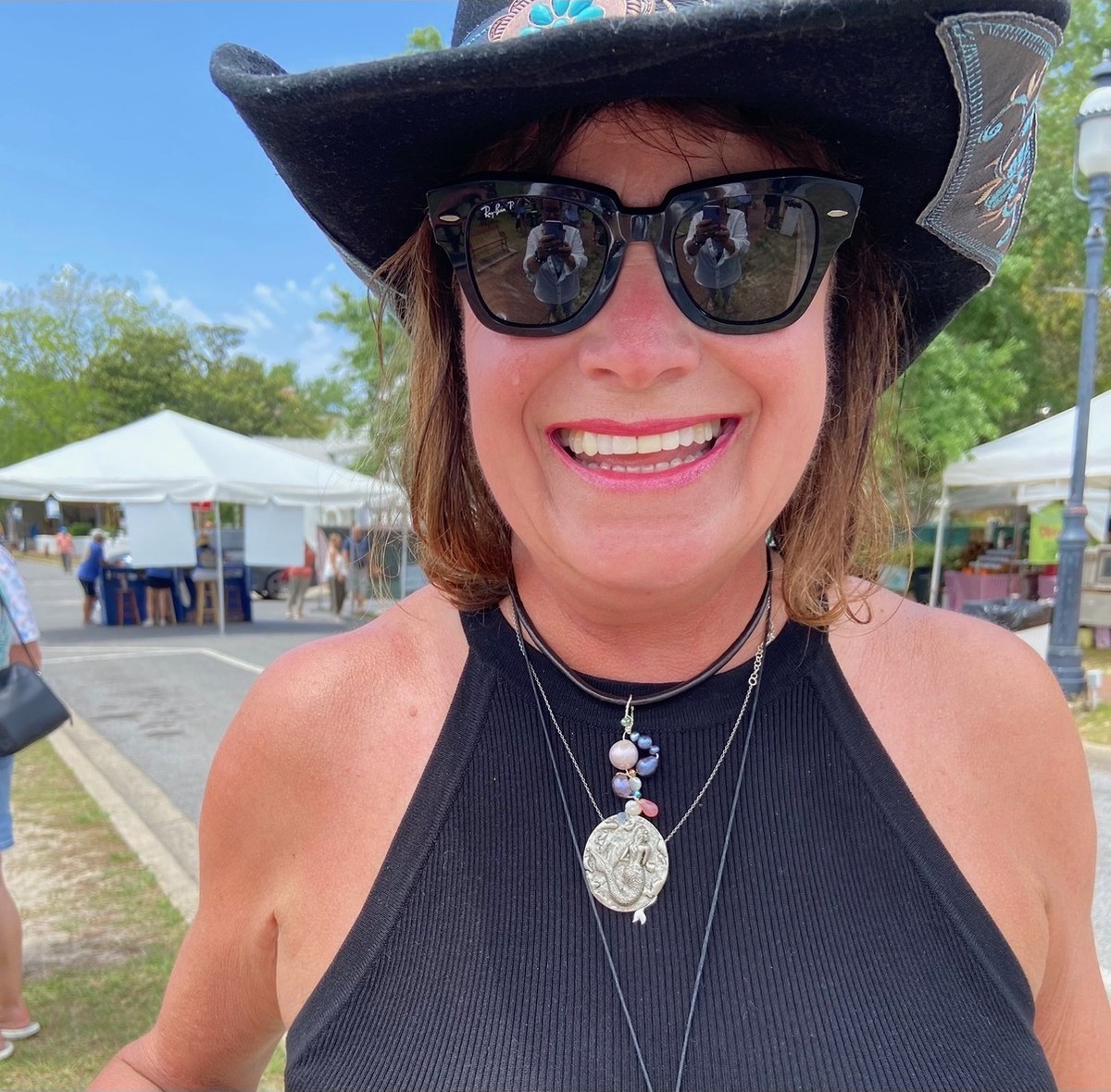 A customer smiling in a black hat and a mermaid medallion pearl necklace