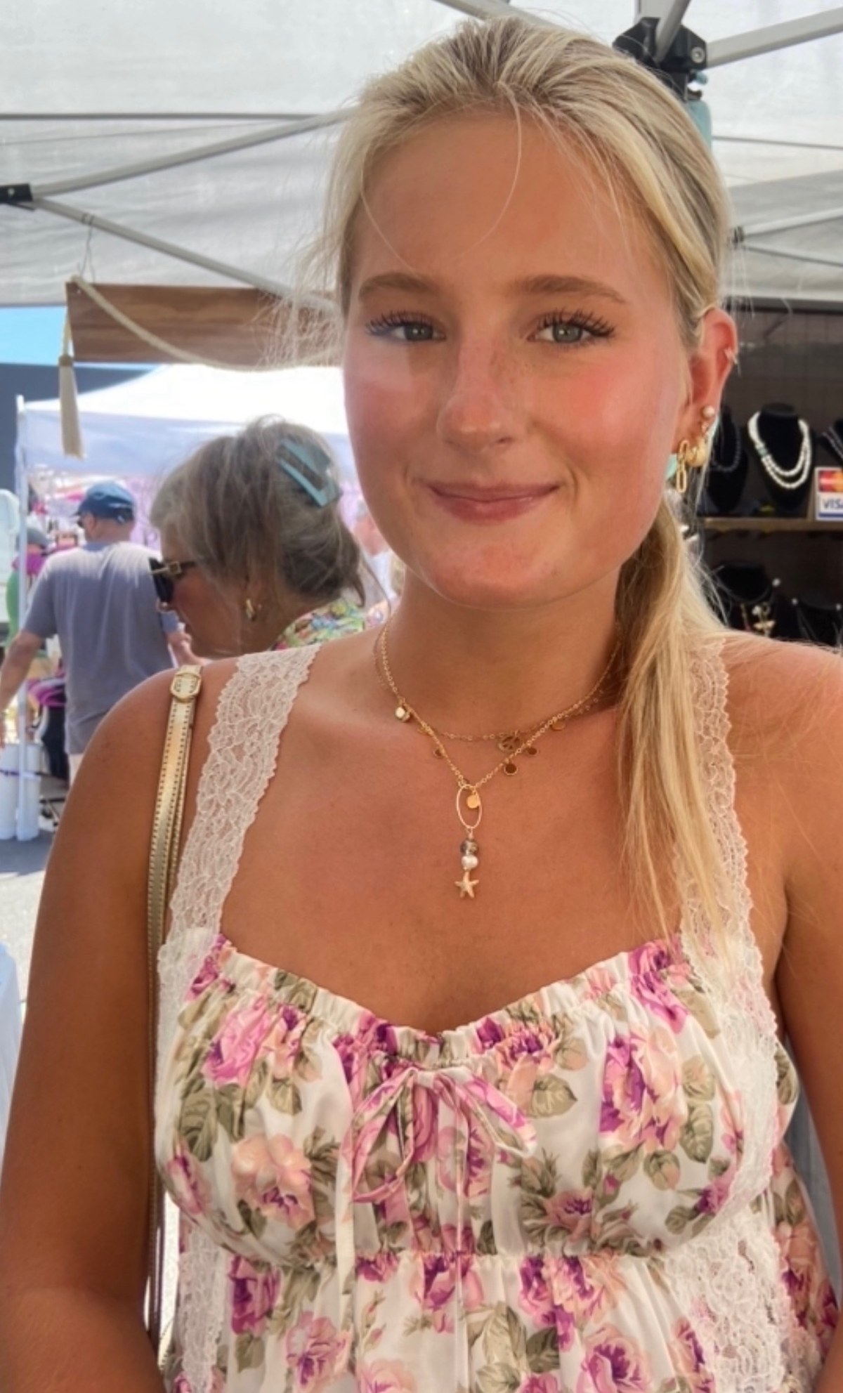A customer wearing layered gold and pearl necklaces at a summer festival