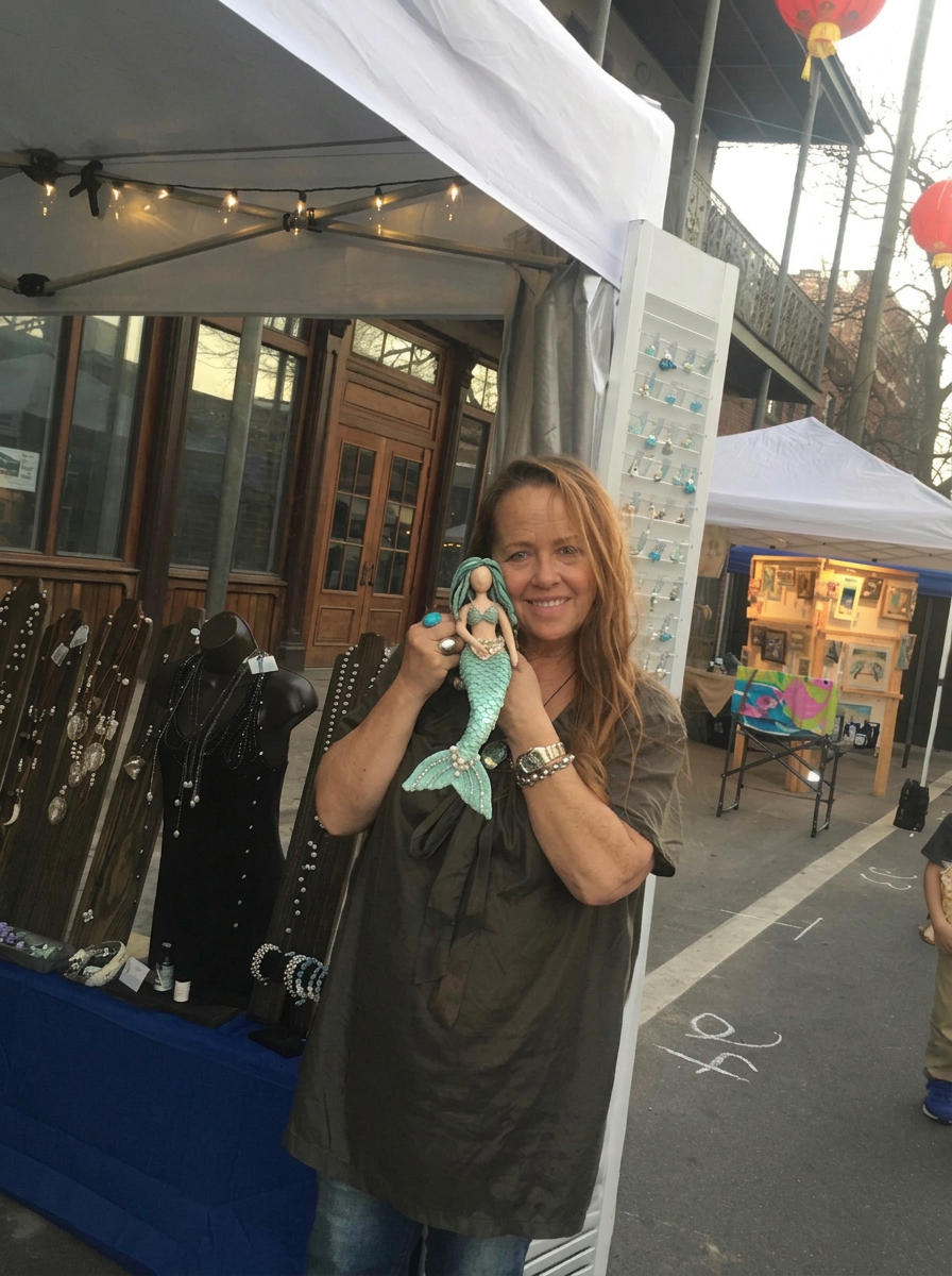 Suzie smiling with a handcrafted mermaid at her festival booth